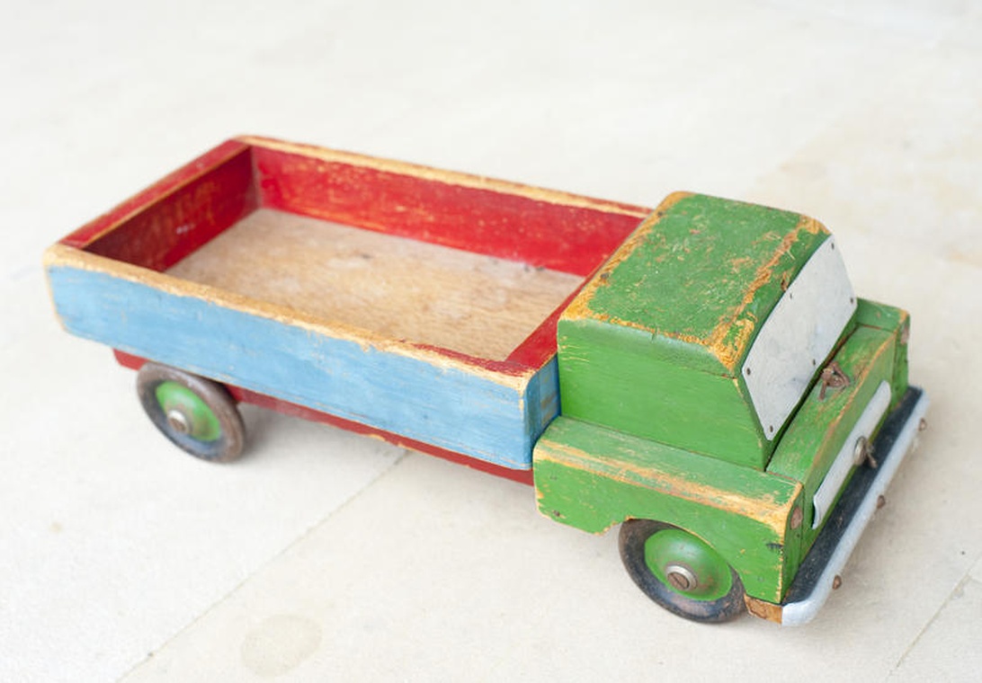 Een handgemaakte houten speelgoedvrachtwagen met groene cabine en blauw-rode laadbak.